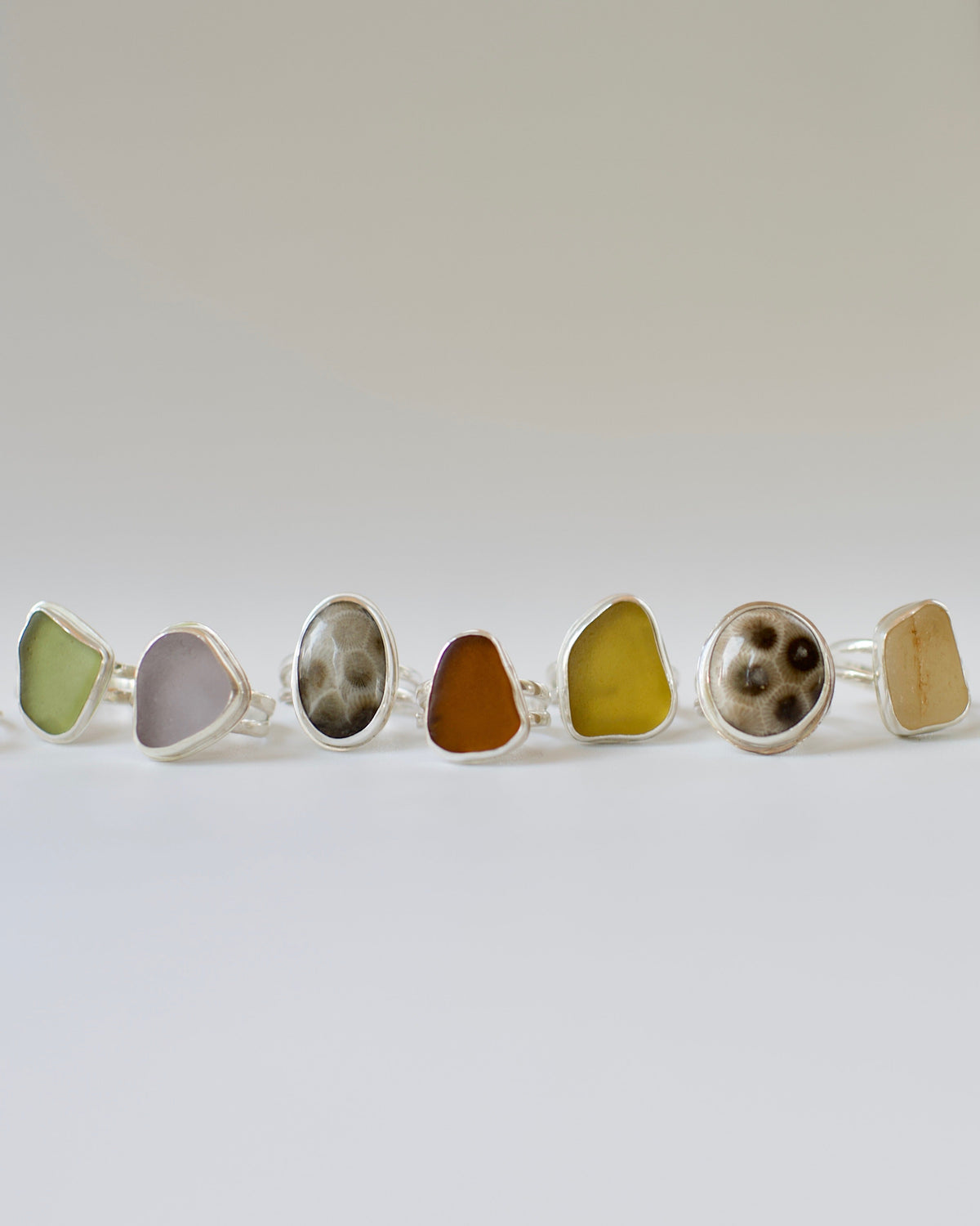 Row of sea glass  and petoskey stone rings on a white background