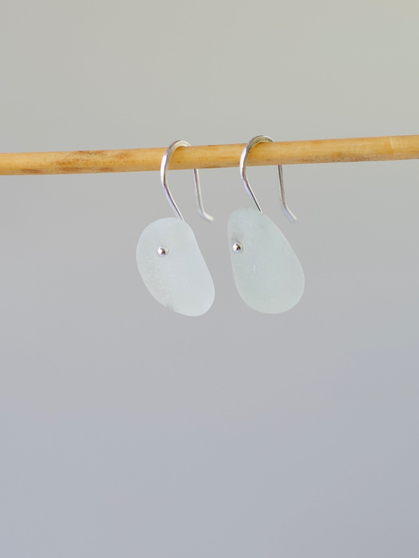 Pair of light aqua beach glass earrings on a wooden rod against a gray background