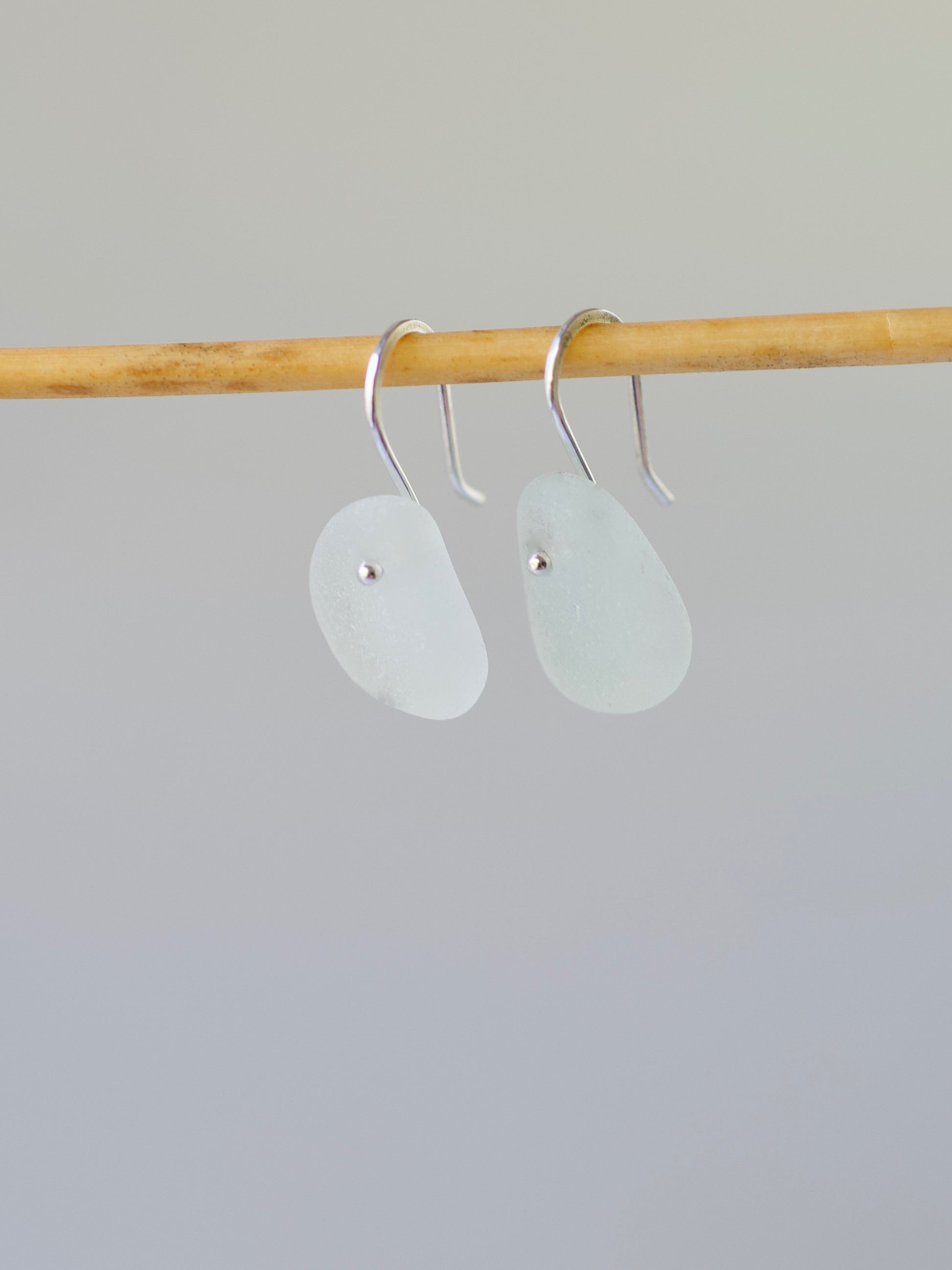 Pair of light aqua beach glass earrings on a wooden rod against a gray background