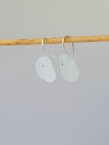 Pair of light aqua beach glass earrings on a wooden rod against a gray background