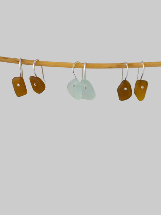 Three pairs of beach glass french wire earrings on a stick against a light gray background