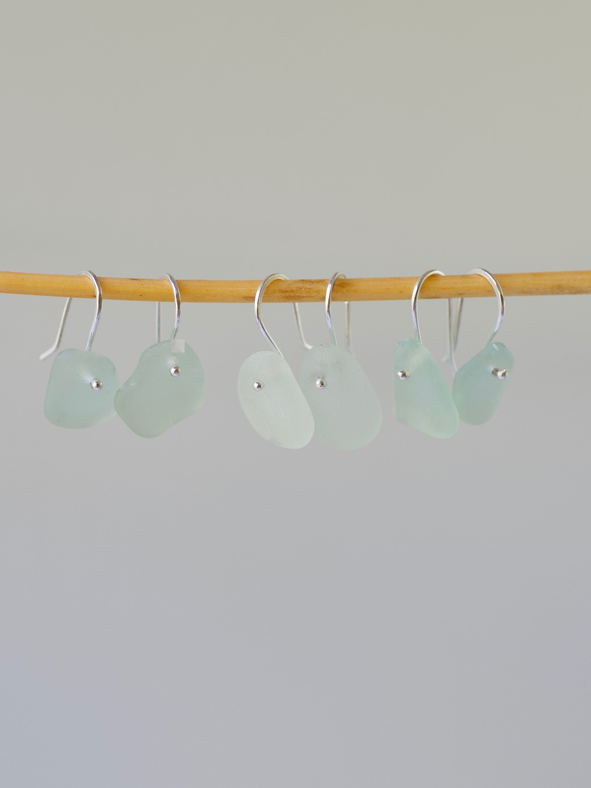 three pairs light aqua beach glass french ear wire earrings on a wooden rod against a gray background