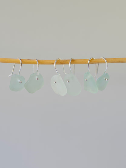 three pairs light aqua beach glass french ear wire earrings on a wooden rod against a gray background