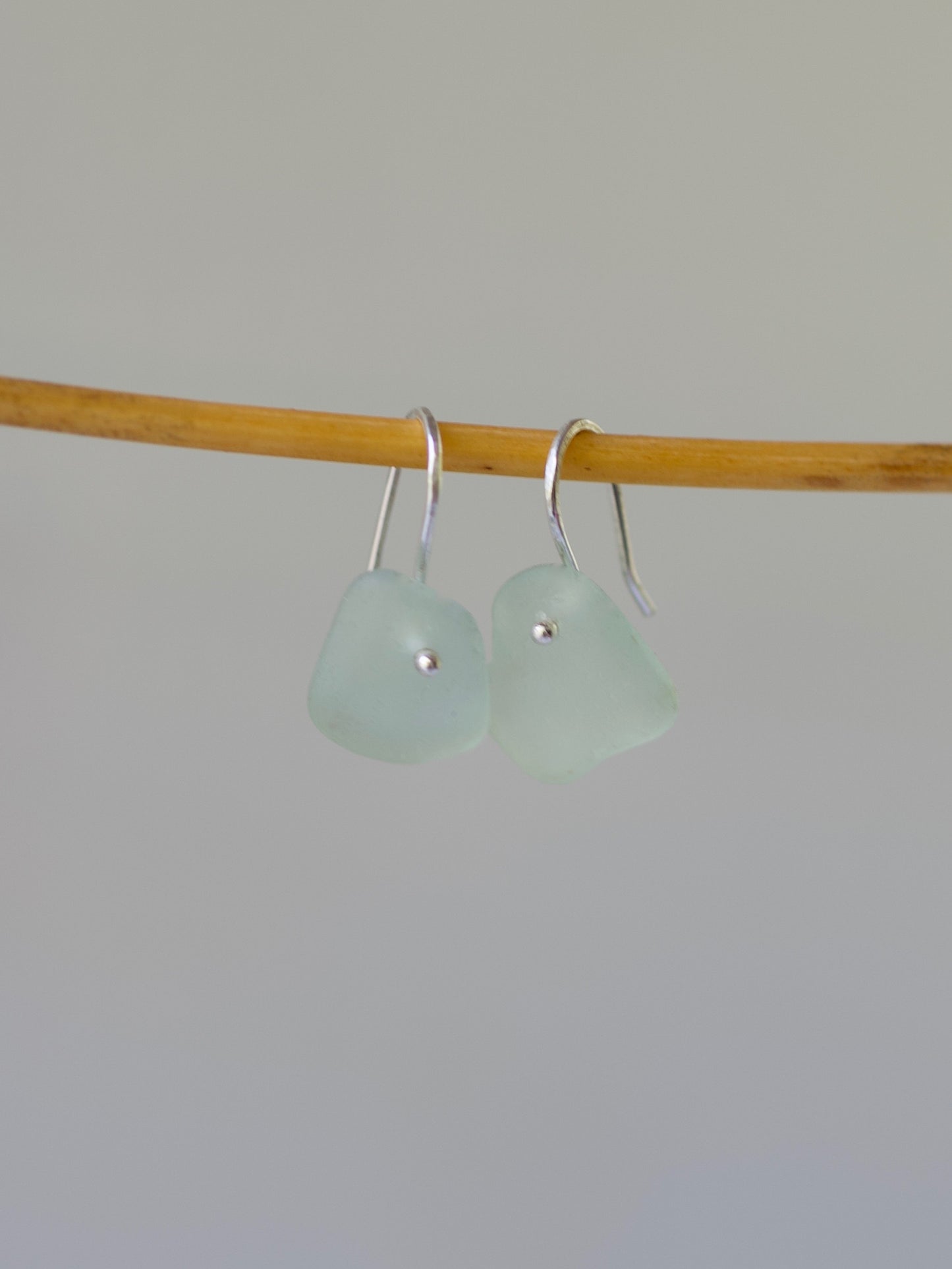 Pair of light green sea glass earrings on a stick against a plain background