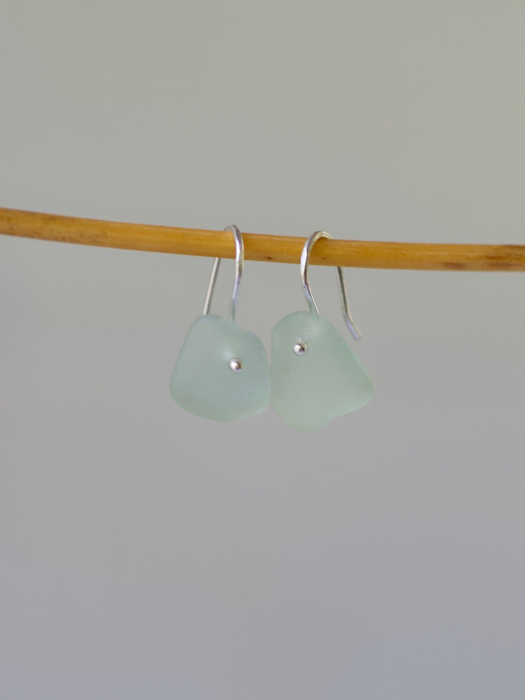 Pair of light green sea glass earrings on a stick against a plain background