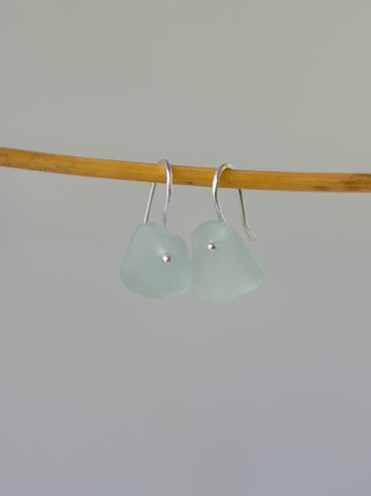 Pair of light green sea glass earrings on a stick against a plain background