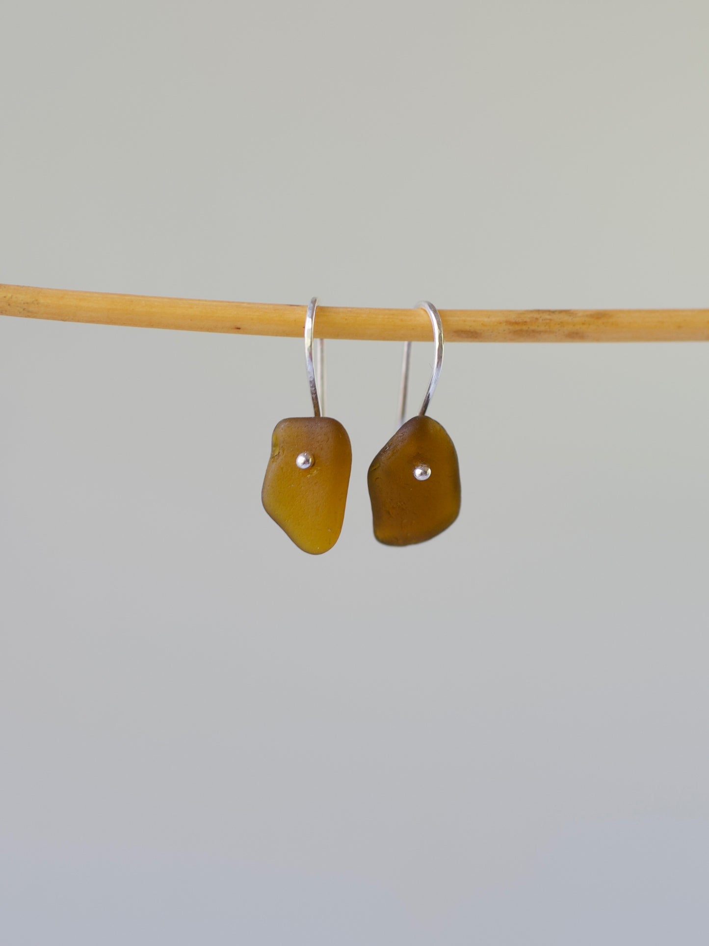 Pair of amber-colored sea glass earrings on a bamboo stick against a gray background
