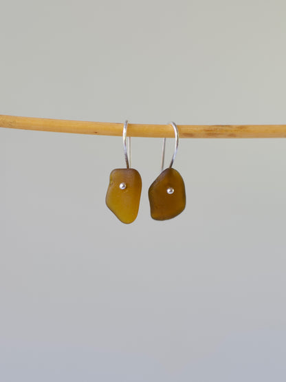 Pair of amber-colored sea glass earrings on a bamboo stick against a gray background