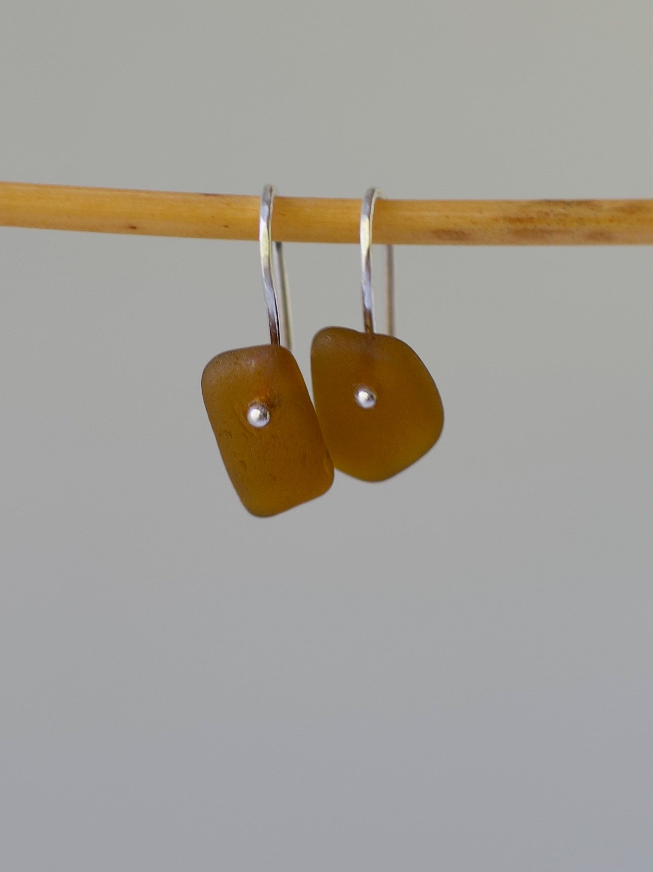 Pair of amber-colored sea glass earrings on a bamboo stick against a gray background